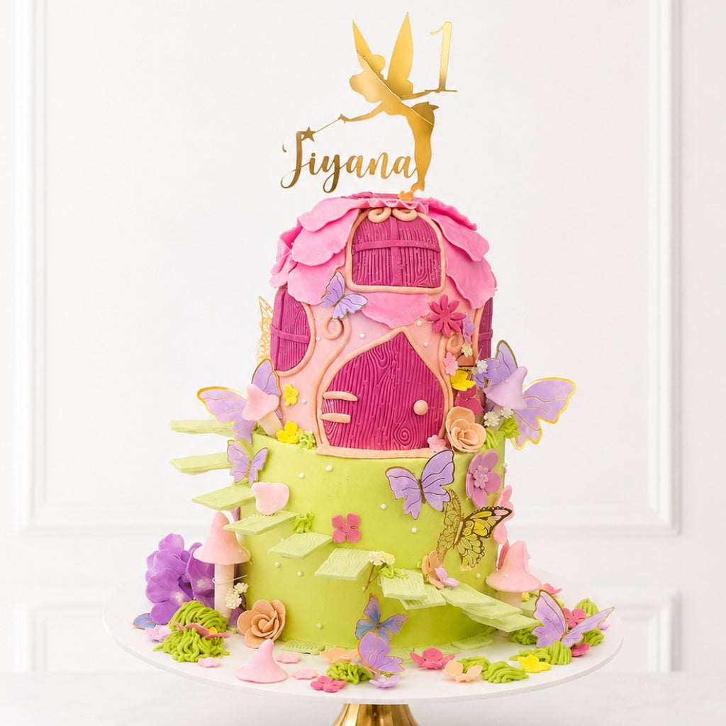 Colorful fairy house cake with pink door and green base, decorated with butterflies and flowers, on a white background.
