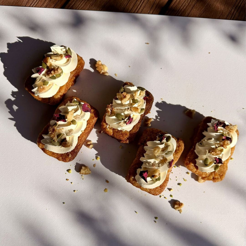 Five small desserts with cream and toppings on a white surface with shadows.