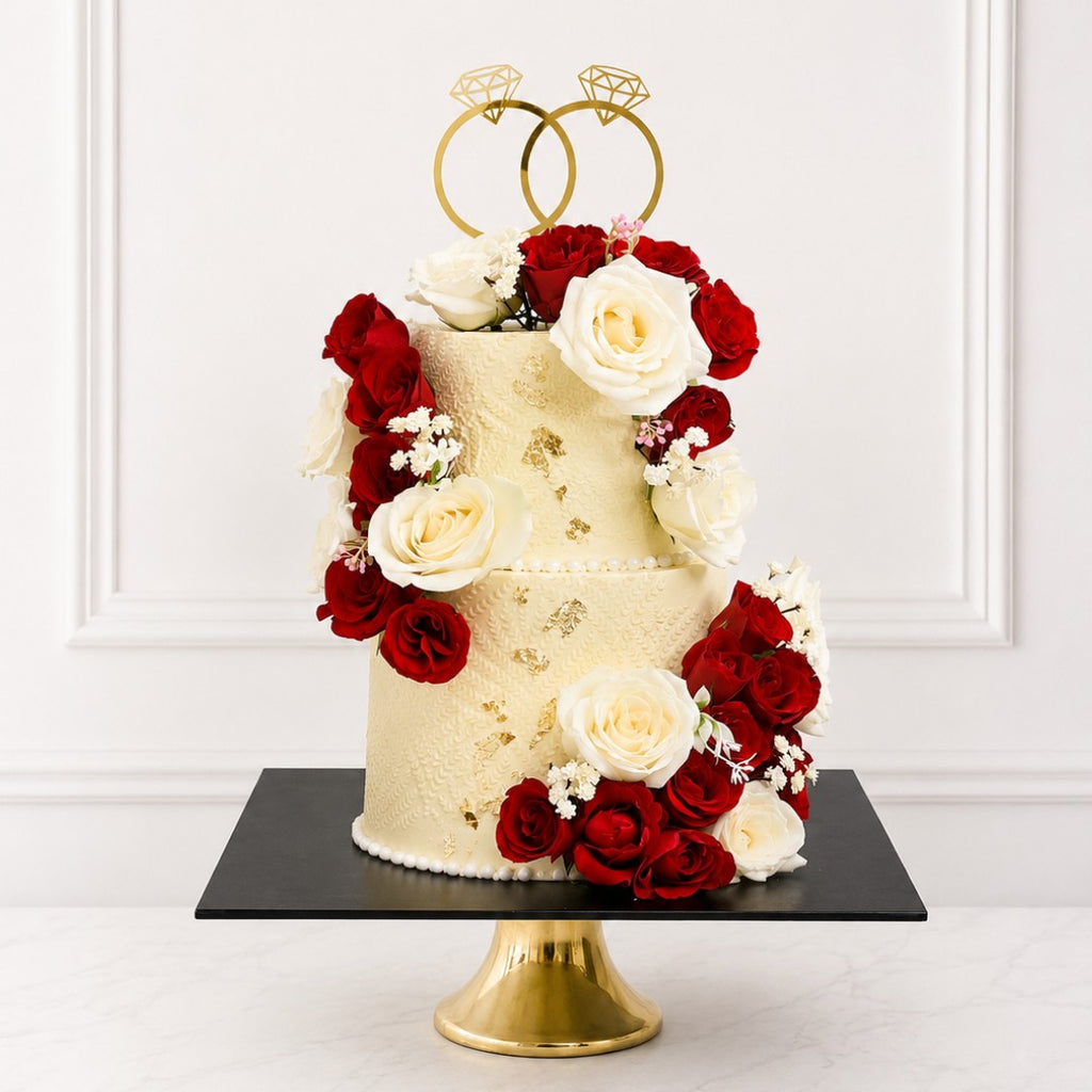 Two-tier wedding cake with red and white flowers and gold ring decorations on a white background