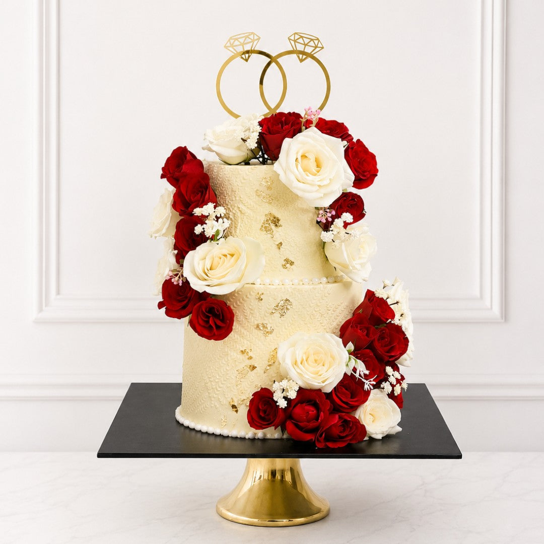 Two-tier wedding cake with red and white flowers and gold ring decorations on a white background